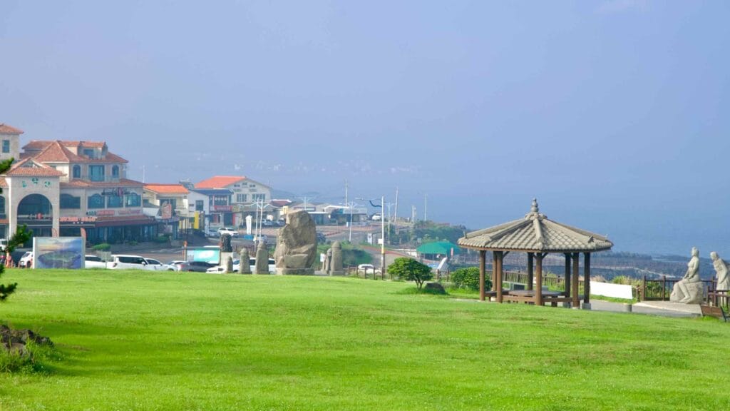 Park lawn with a pavilion and stone sculptures overlooks a seaside village near Songaksan.