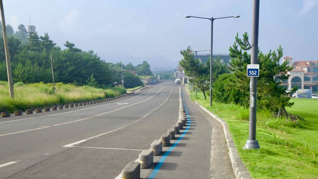 A blue‑striped bike lane follows the coastal road through Daejeong‑eup near Songaksan.