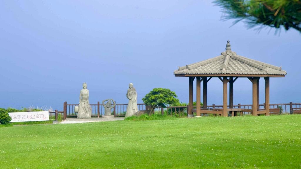 Stone statues inspired by Jeju’s haenyeo female divers stand beside a pavilion.