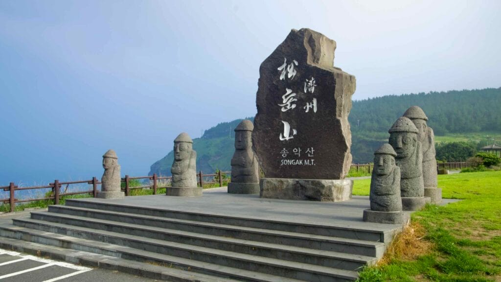 A marker carved “Songak M.T.” stands with a row of dol hareubang guardian statues.