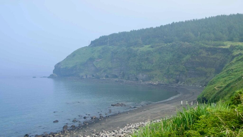 The dark‑sand cove beneath Songaksan curves below green cliffs.