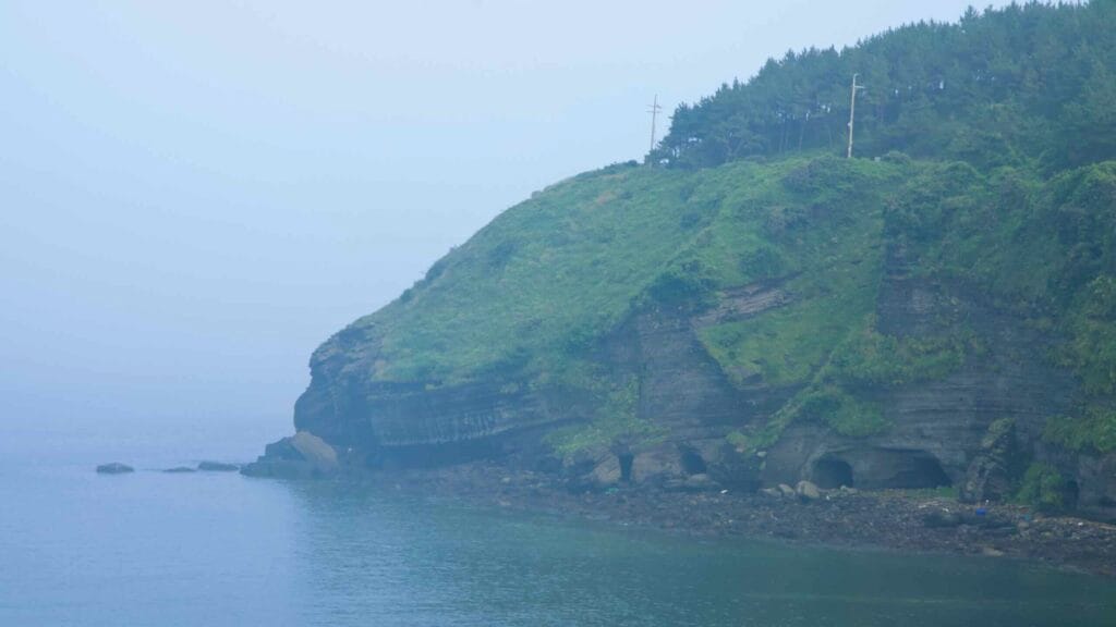 Banding and small sea caves are visible in the basalt cliffs at Songaksan headland.