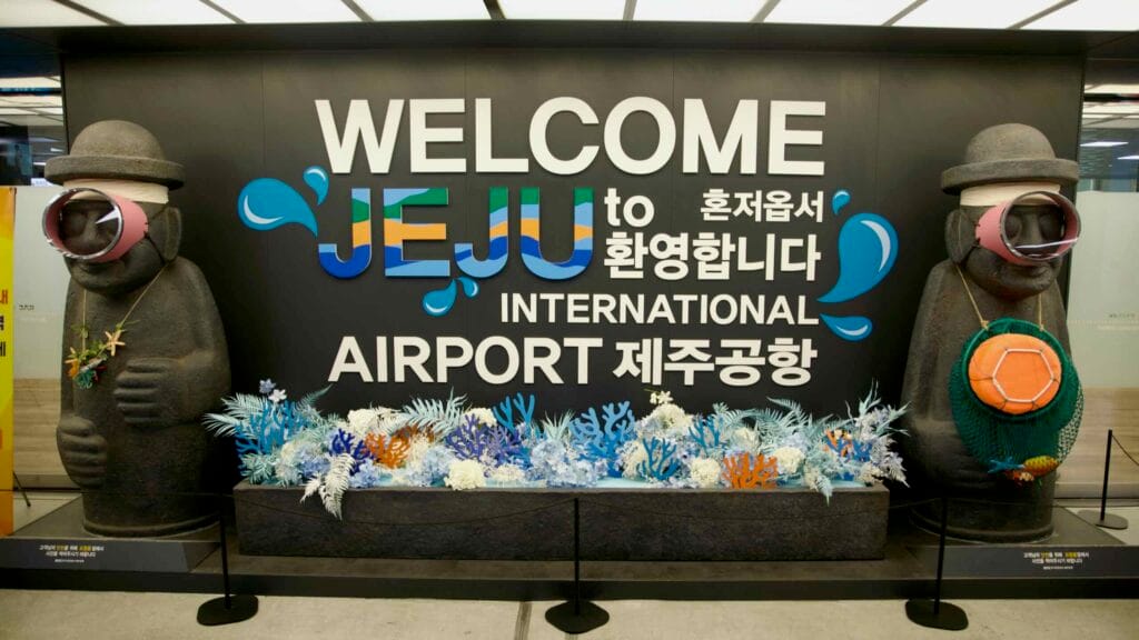 “WELCOME JEJU” sign with dolhareubang statues inside Jeju International Airport.