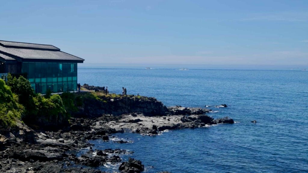 Glass‑walled café on Aewol’s basalt cliffs above the blue Korea Strait.
