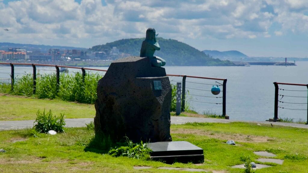 Seated mermaid statue beside the coastal path at Eoyeong Park.