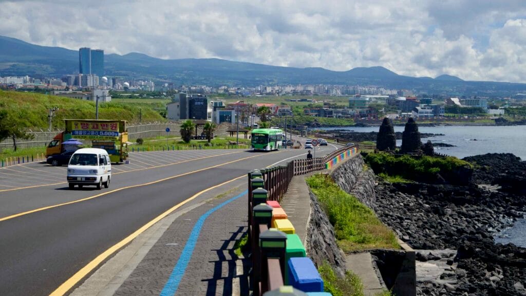Green city bus on the rainbow‑fenced coastal road near Sasu Port.