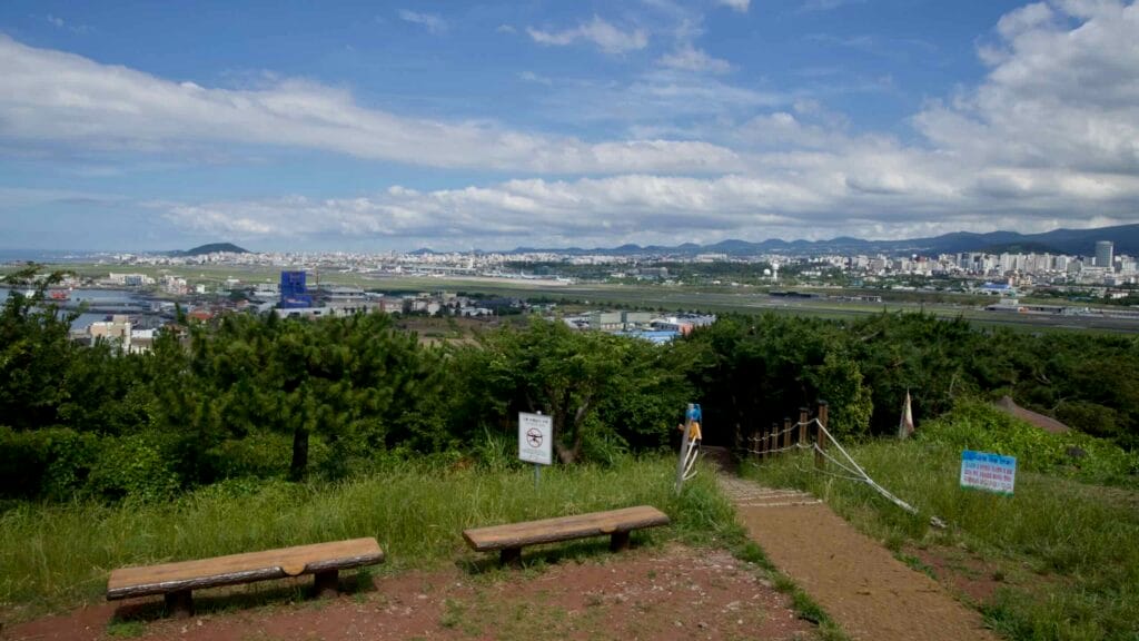 Hilltop benches and a path above the runway—panoramic view across Jeju Airport.
