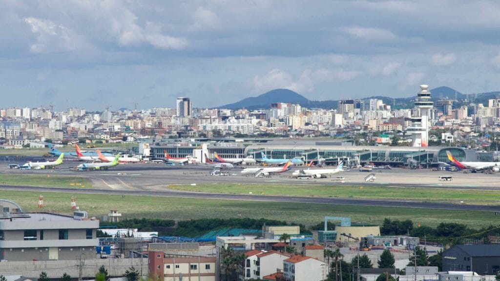 A busy apron at Jeju International: tails lined up beneath thick summer clouds.