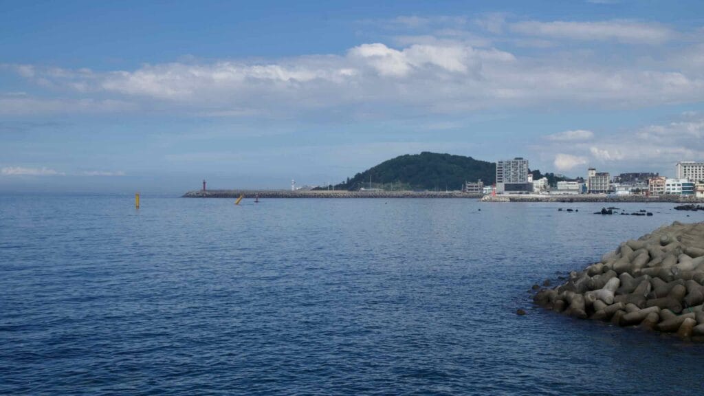 A view across calm water toward Iho Port’s long breakwater and low hills.
