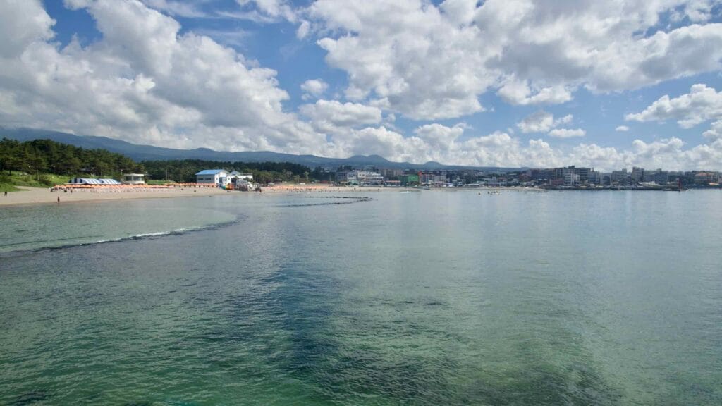 Wide view across Iho Tewoo’s clear bay toward Jeju City.