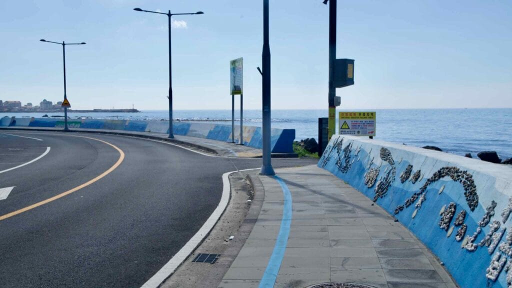Curving seawall and blue‑striped coastal path by the sea.