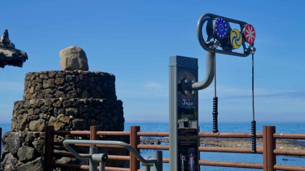 Seaside fitness equipment beside a stone beacon.