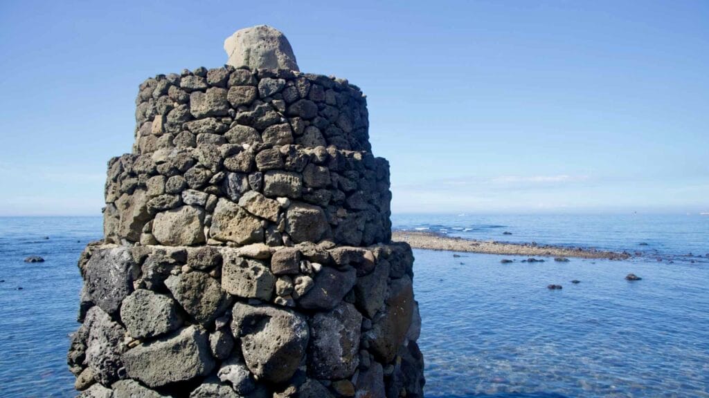 Tiered lava‑stone beacon at the water’s edge.