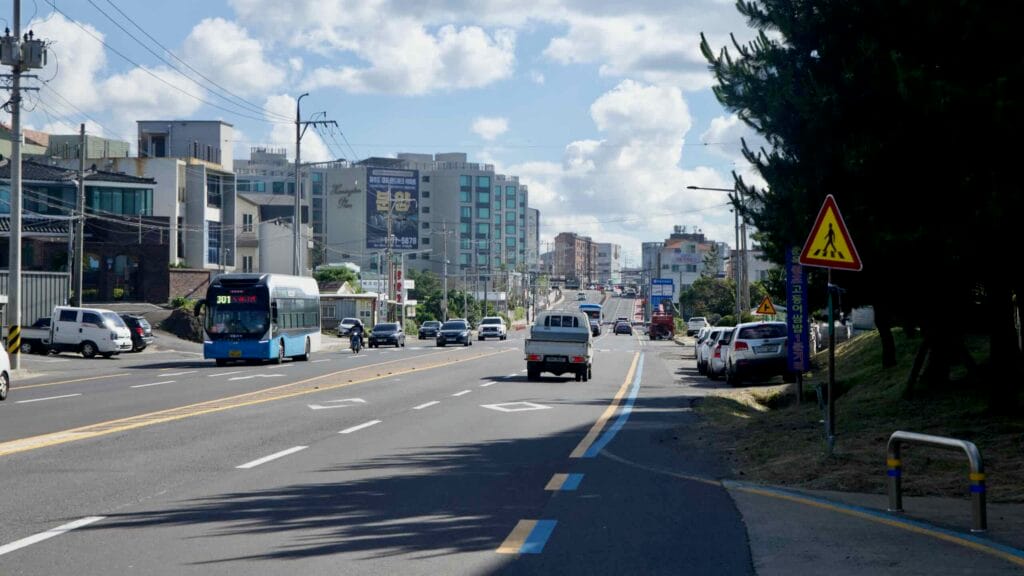 Traffic flows along a multi‑lane Jeju City artery.