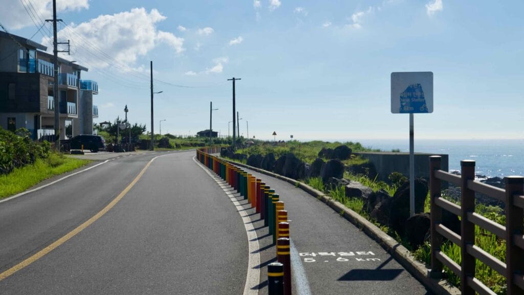 Curving coastal road with colorful posts and bike lane toward Gueom Port in Aewol.