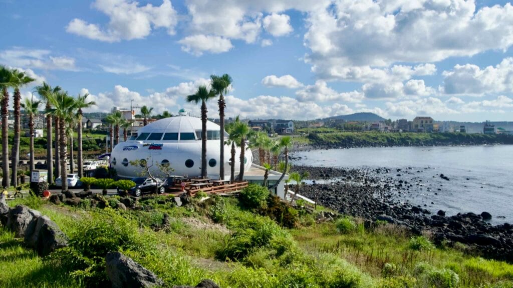 UFO‑shaped café and palms above the rocky Aewol shore on Jeju’s west coast.