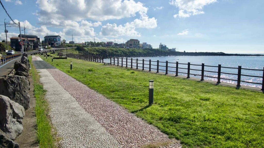 Pebbled foot‑massage path and lawn along the seawall at Darak Coastal Park.