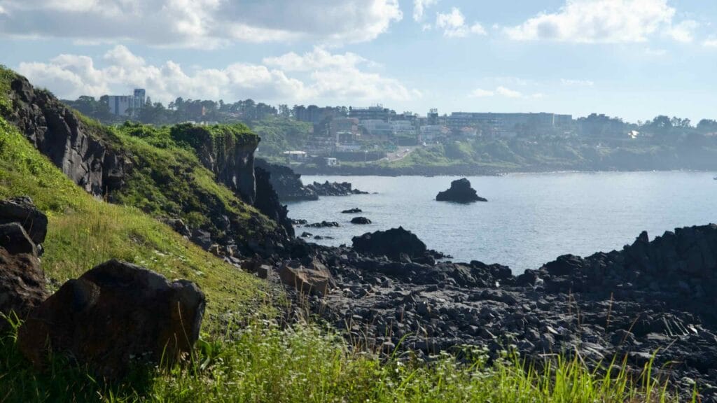 Lava cliffs and boulders above a calm bay near Gueom Port.