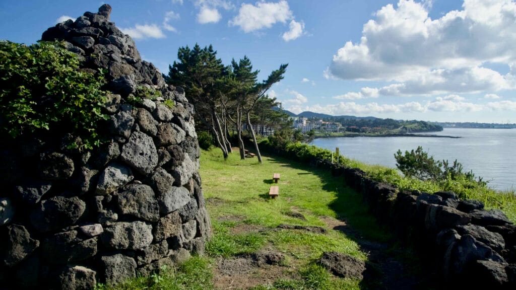 Round stone wall and benches on a grassy bluff above the Aewol bay.