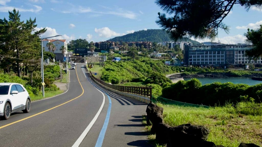 Traffic follows the Hagu‑Aewol Coastal Road past hotels and forests.