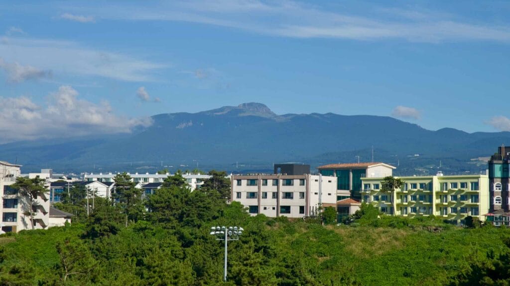 Mount Hallasan rises over Jeju’s interior beyond low apartment near Aewol coast.