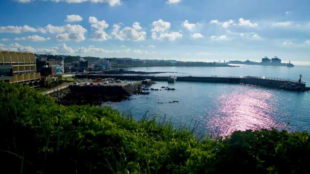 Afternoon light glints across the bay at Gonae Port, where the arc of the breakwater.