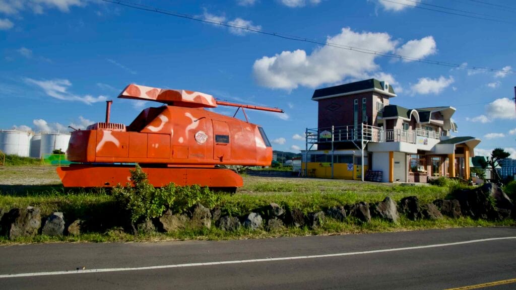 An orange amphibious vehicle display sits beside homes near Aewol Port.