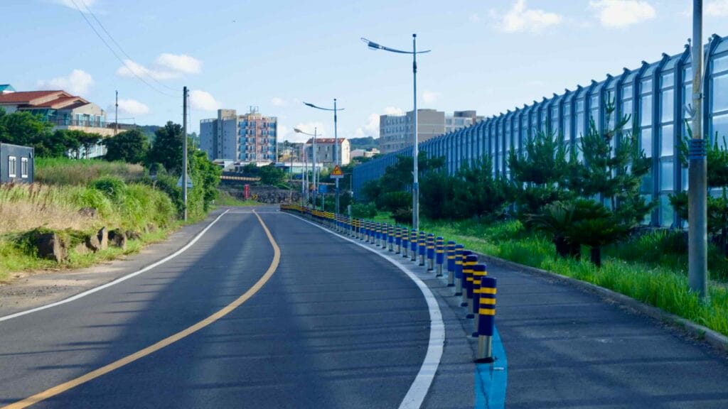 A curving coastal road runs beside a tall glass noise barrier near Aewol Port.
