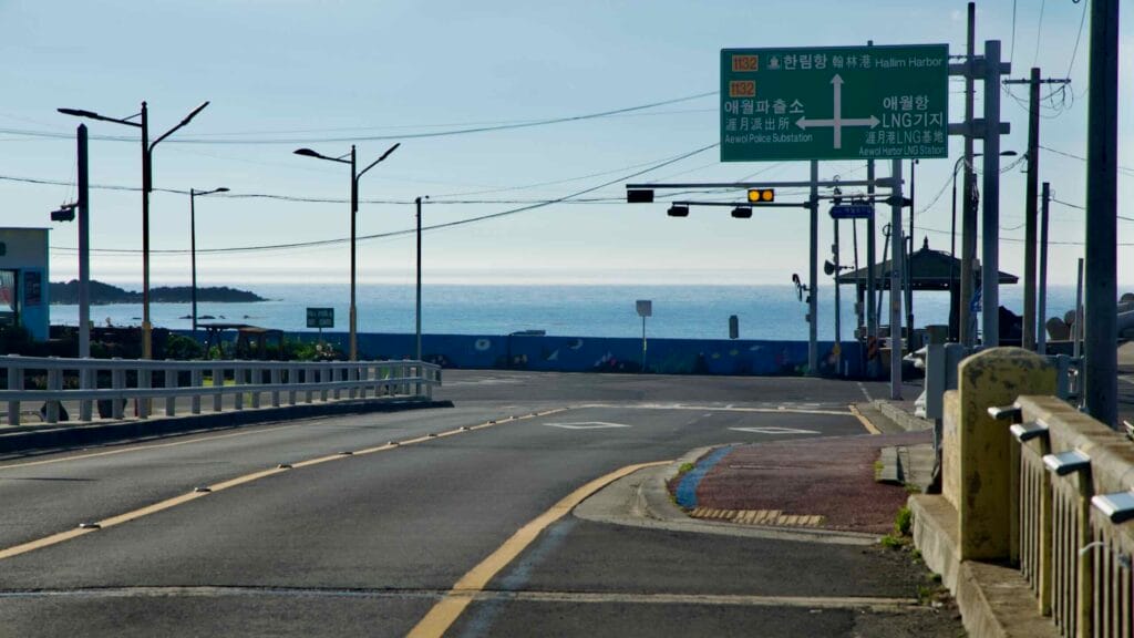 A road junction near Aewol Port faces the sea, with blue mural seawalls.