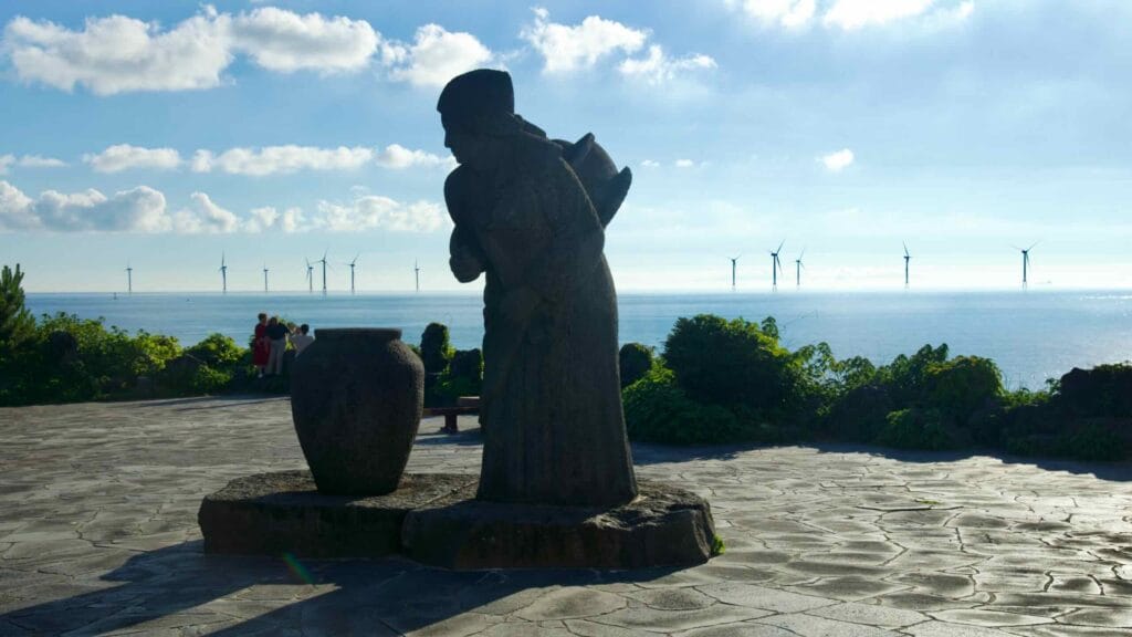 A statue of a woman with a water jar stands at a lookout near Aewol Handam Park.