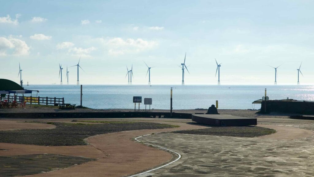 A plaza path at Gwakji Beach leads toward the beach, with offshore wind turbines.