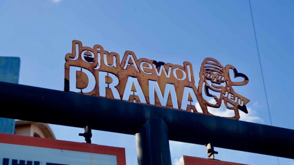 Close view of a weathered metal sign reading Jeju Aewol DRAMA near Gwakji Beach.