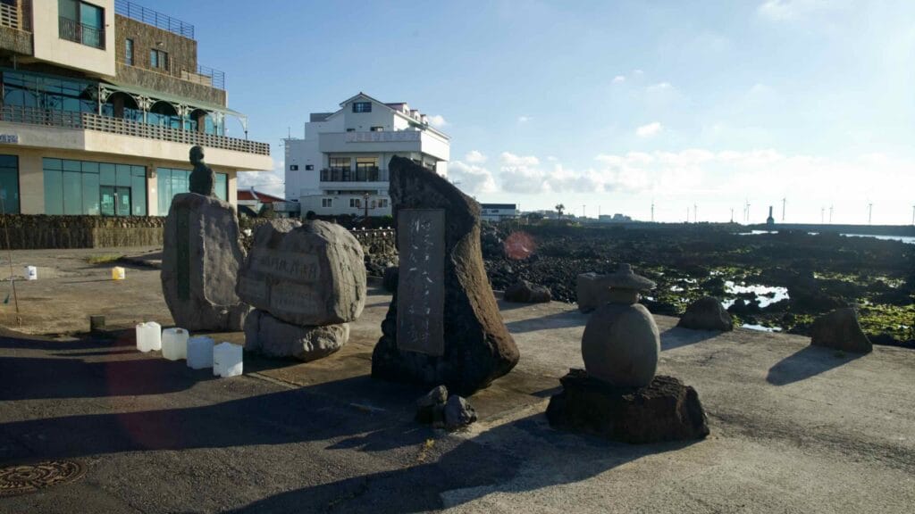 Basalt monuments on the seafront near Gwideok Port with turbines on the horizon.
