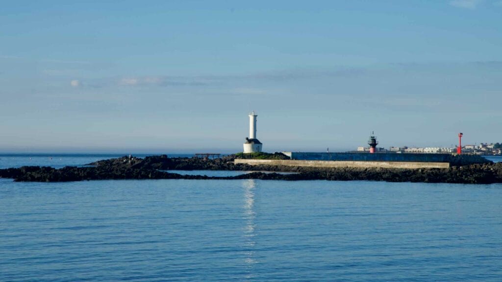 White lighthouse on the breakwater at Gwideok Port under calm blue skies.