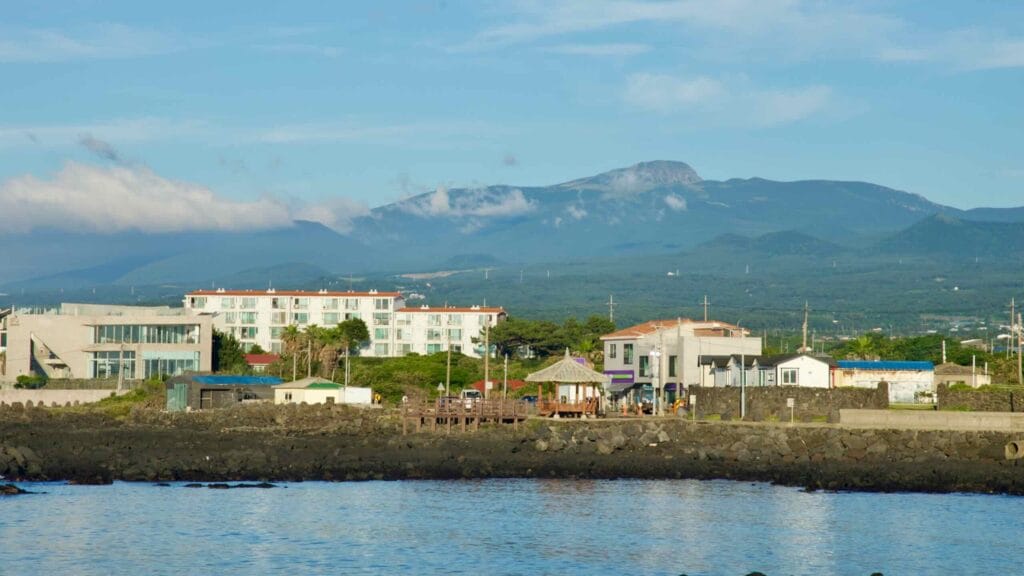 Gwideok Village with Hallasan rising inland beyond the seaside rooftops and pavilion.