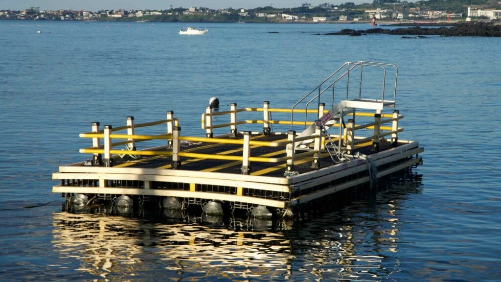 Floating dock near Hansupul Haenyeo School with yellow railings reflected on the water.
