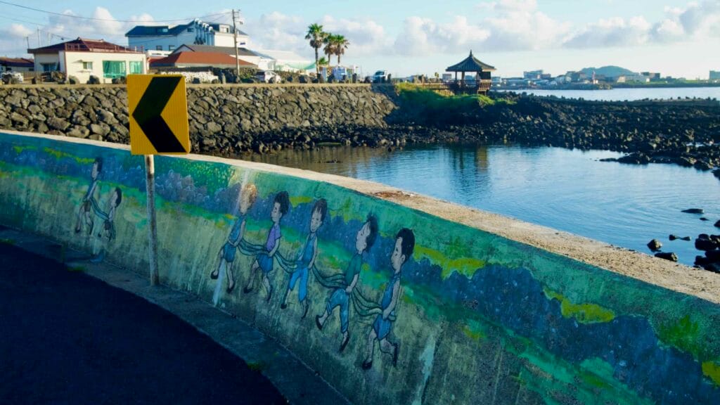 Chevron sign and mural sea wall at Gwideok’s quay with pavilion beyond.