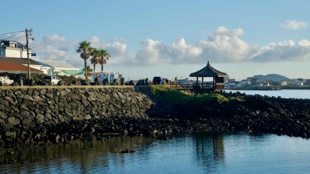 Wooden pavilion above the basalt seawall at Gwideok with harbor views.