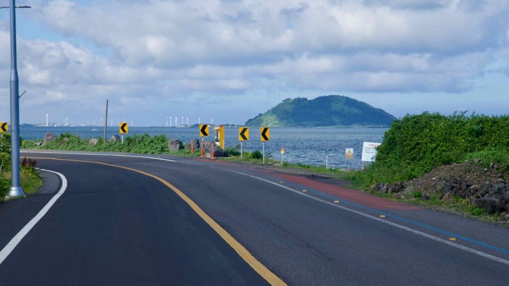 A coastal road marked with signs follows the shoreline toward green Biyangdo Island.