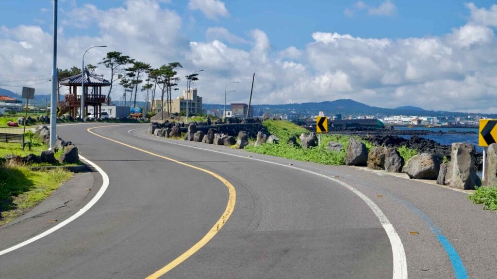 A curving seaside road and blue-striped bike lane pass basalt boulders.