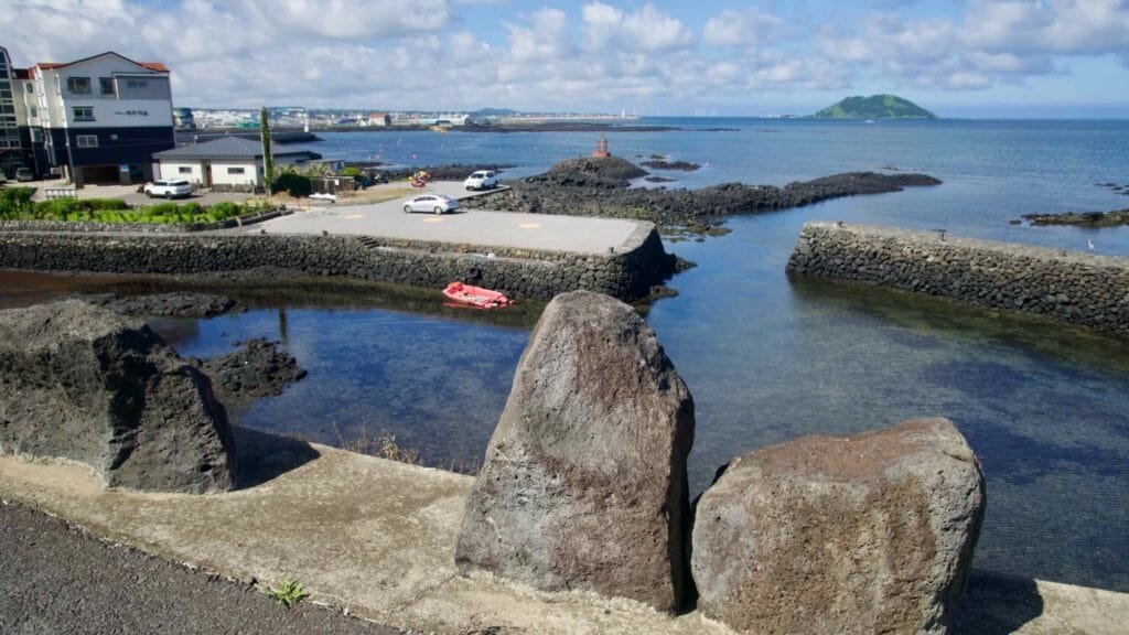 A lava-rock quay leads to a small beacon as Biyangdo Island rises beyond the bay.
