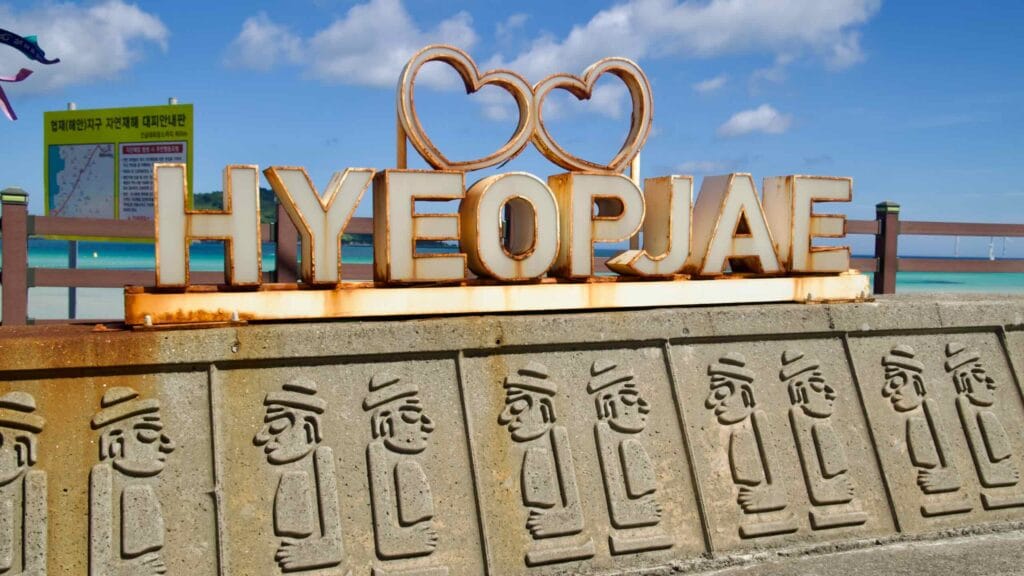 HYEOPJAE sign above hareubang relief seawall beside the beach.
