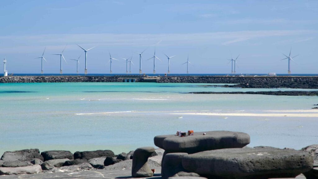 Basalt tables face turquoise shallows and breakwater windmills at Hyeopjae.