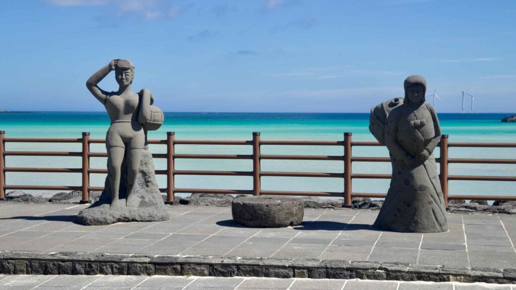 Basalt haenyeo diver statues along the Hyeopjae promenade.