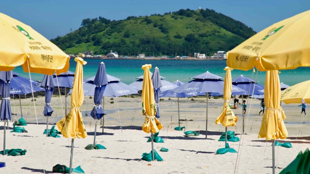 Folded umbrellas on white sand facing Biyangdo’s turquoise channel.