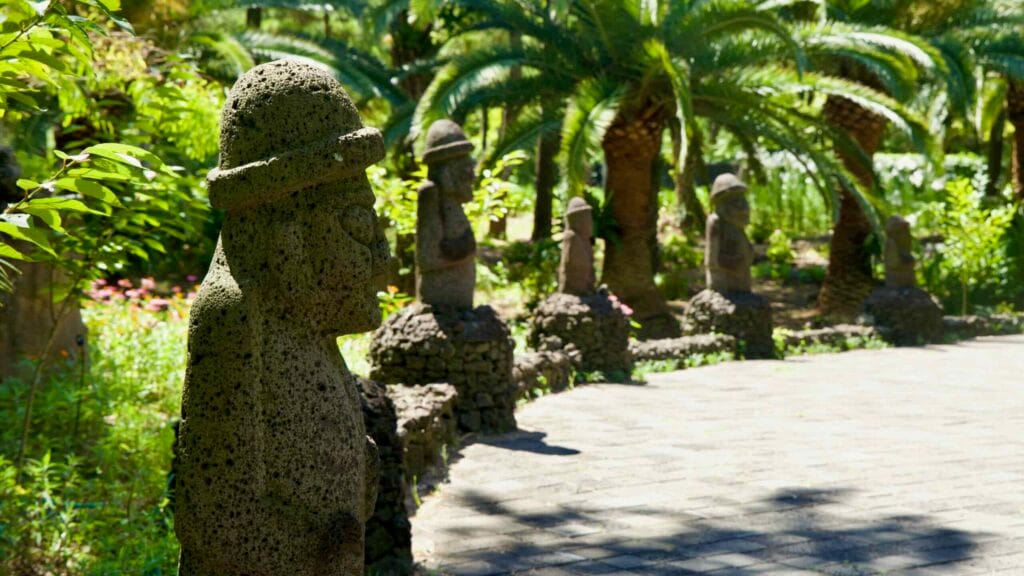 Row of basalt dol hareubang statues bordering a garden path.