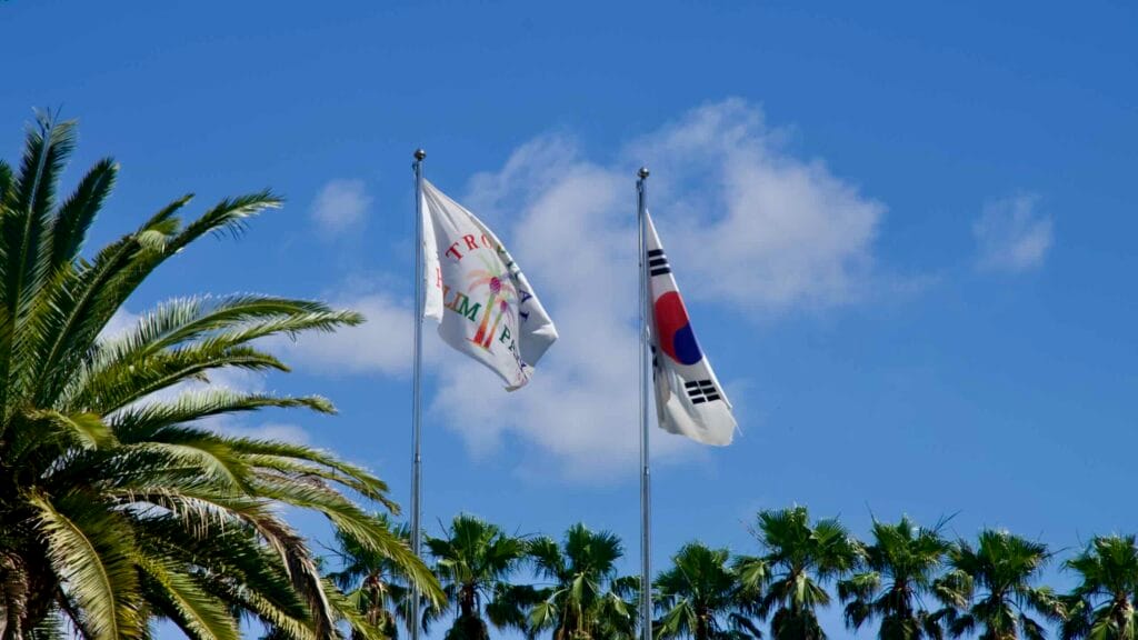 Korean and Hallim Park flags flying above palms on a clear day.