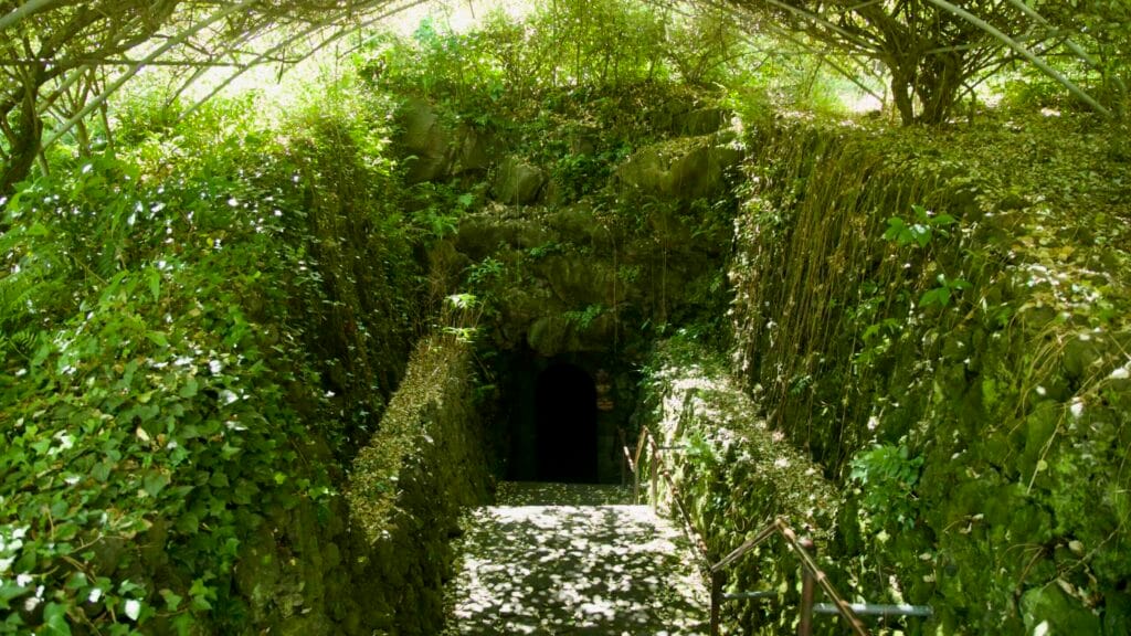 Leafy trellis and stone steps lead down to the Hallim Park lava cave entrance.