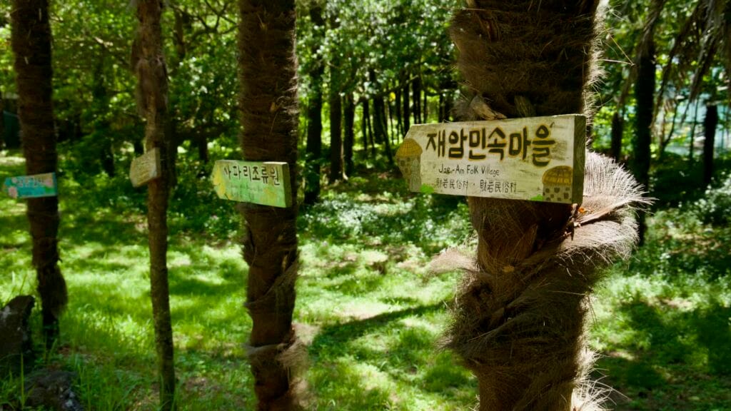 Hand‑painted sign pointing to Jae‑Am Folk Village inside Hallim Park.