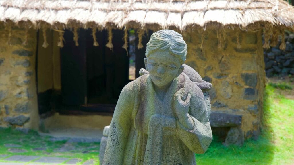 Stone statue of a woman by a thatched house in Hallim Park’s folk village.
